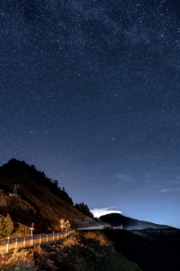星空下的高山公路，車燈拖出光軌