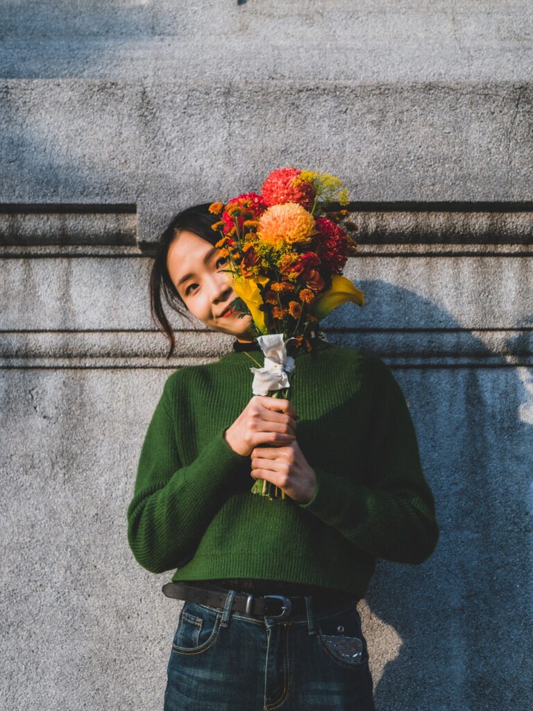 石牆前捧花、閉眼微笑的女子
