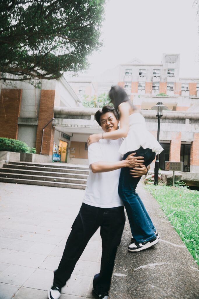 男生把女生抱起，背景是紅磚建築