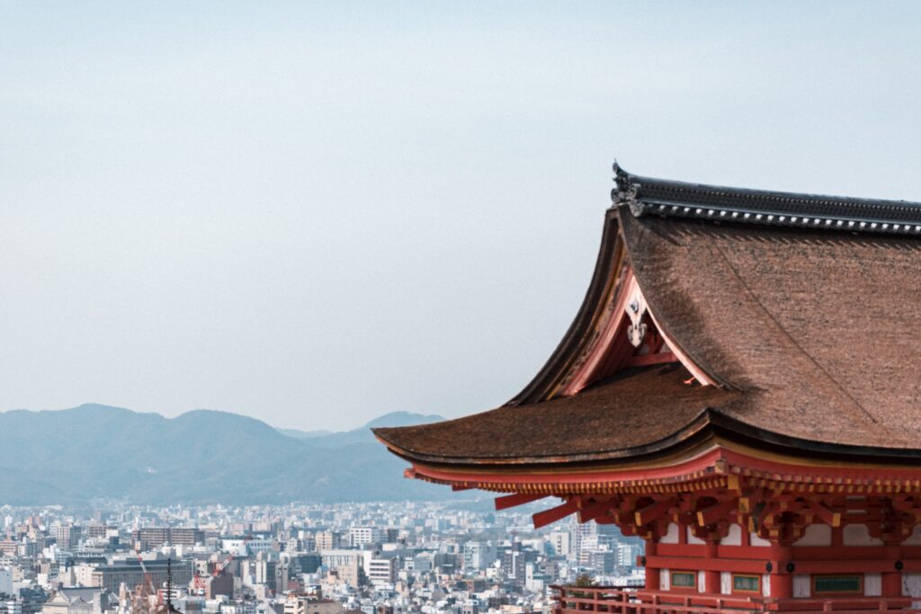 朱色寺院屋簷伸出畫面，後方是京都市區與遠山