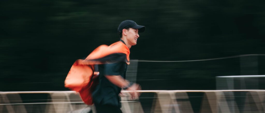穿學士服、背橘色背包的畢業生快步走過，背景拉成流動的線條