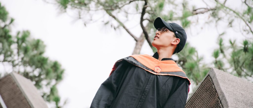 仰角拍攝穿學士服的畢業生，背後是松樹
